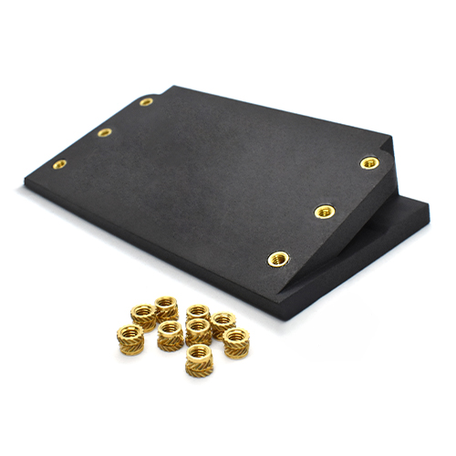 Black block object with six brass threaded inserts, also pile of inserts sitting in front