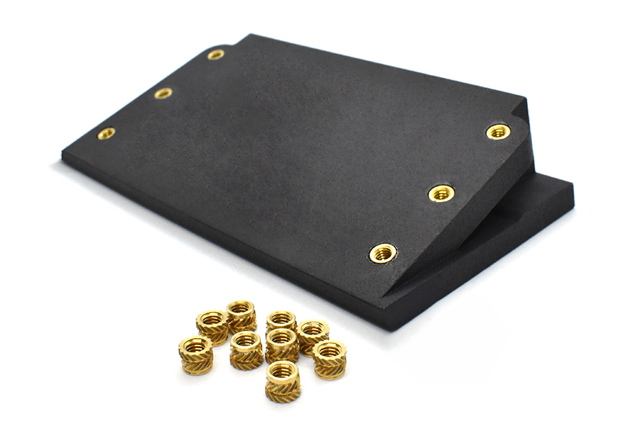 Black plastic block with gold threaded inserts scattered in front 