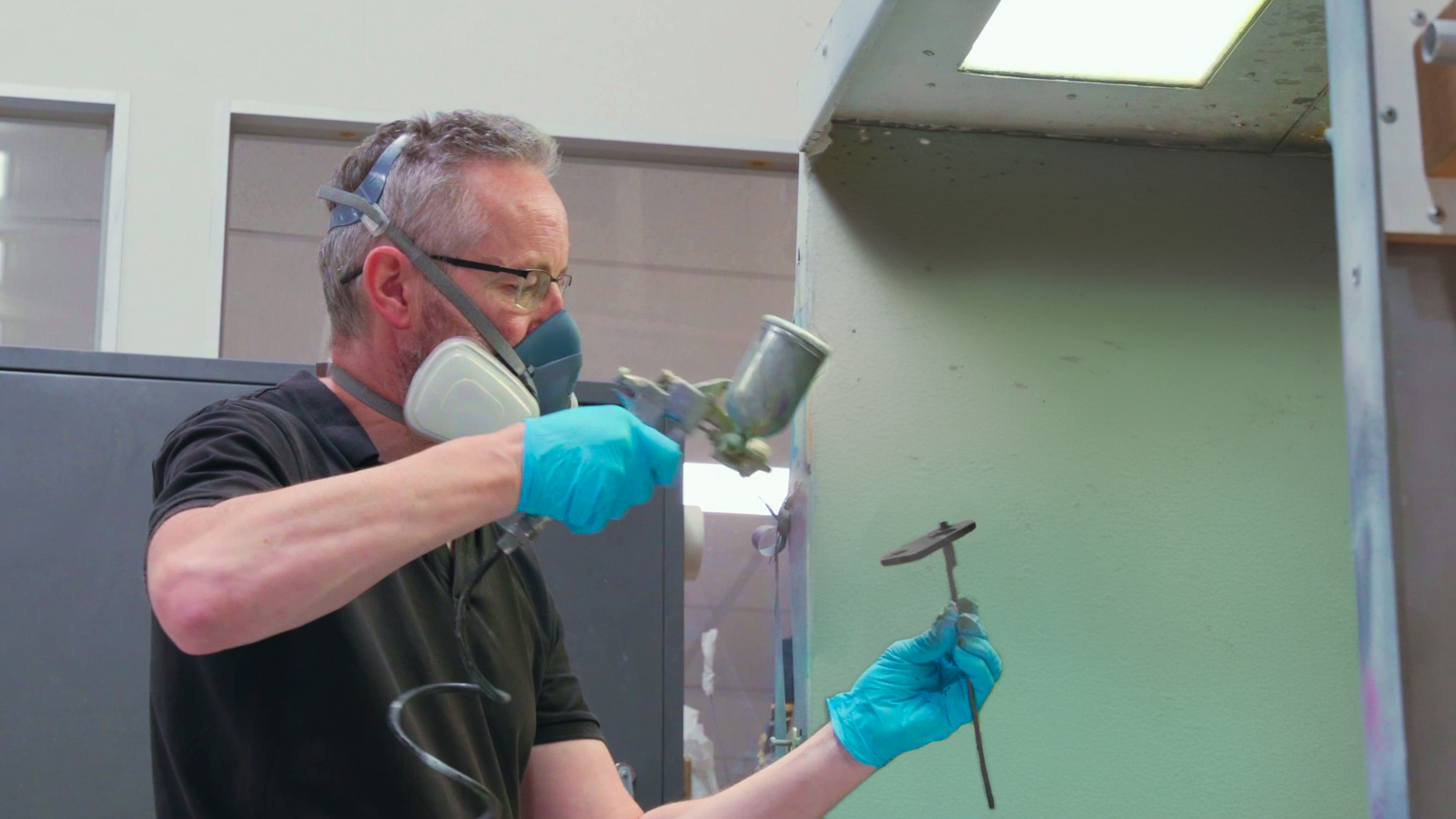 Man with blue gloves spray painting small part in black