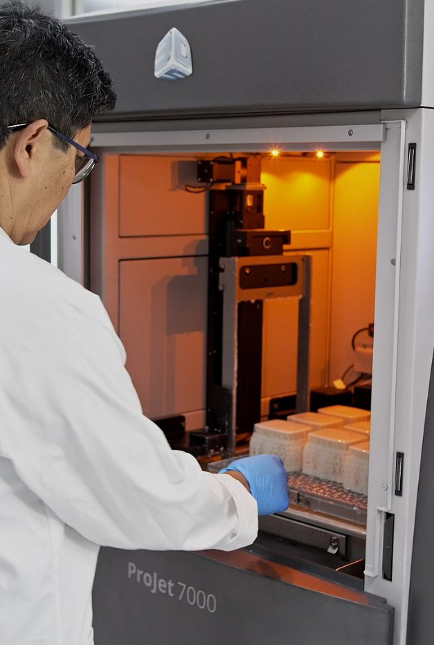 Man in white coat reaching into 3d printing machine